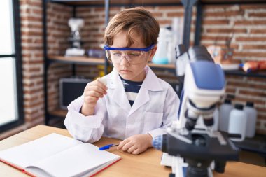 Adorable hispanic boy student looking sample at laboratory classroom