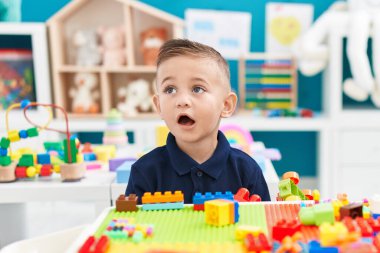 Adorable hispanic boy playing with construction blocks standing at kindergarten