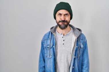 Young hispanic man with tattoos wearing wool cap puffing cheeks with funny face. mouth inflated with air, crazy expression. 