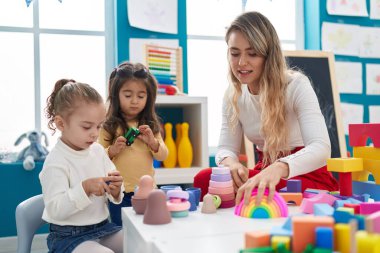 Teacher with girls playing with geometry blocks sitting on table at kindergarten