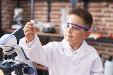 Adorable hispanic boy student looking sample at laboratory classroom