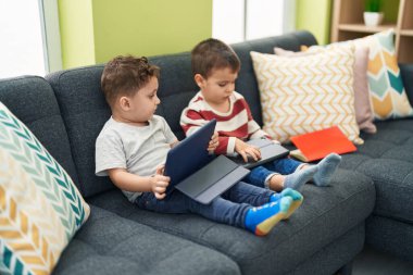 İki çocuk dokunmatik yastıkta video izliyor. Evdeki koltukta oturuyor.