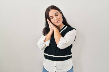 Young hispanic woman standing over isolated background sleeping tired dreaming and posing with hands together while smiling with closed eyes. 