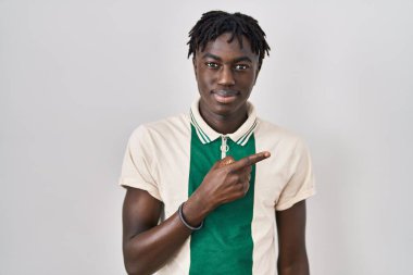 African man with dreadlocks standing over isolated background pointing with hand finger to the side showing advertisement, serious and calm face 