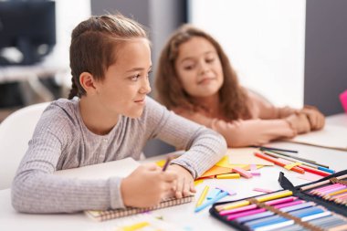 Two kids students sitting on table drawing on notebook paper at classroom