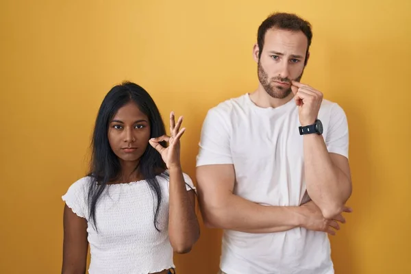 Interracial Couple Standing Yellow Background Mouth Lips Shut Zip Fingers — Zdjęcie stockowe