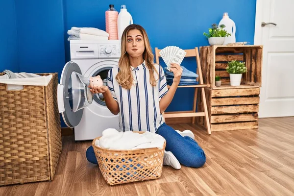 Young blonde woman doing laundry saving money puffing cheeks with funny face. mouth inflated with air, catching air.