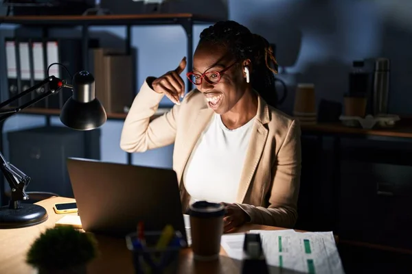 Beautiful black woman working at the office at night smiling doing phone gesture with hand and fingers like talking on the telephone. communicating concepts.