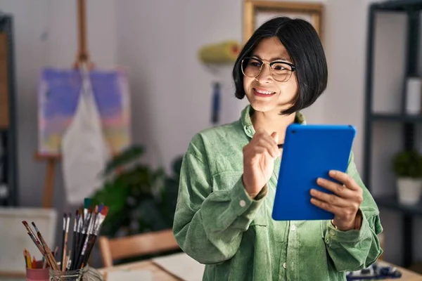 Young chinese woman artist smiling confident using touchpad at art studio