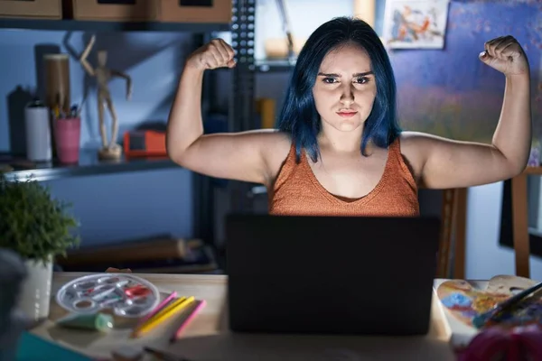 年轻的现代女孩 蓝头发 晚上坐在艺术工作室里 带着笔记本电脑 露出胳膊肌肉 带着骄傲的笑容 健身概念 — 图库照片
