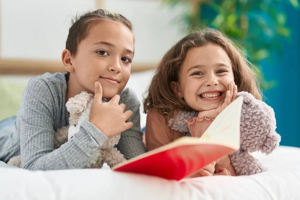 Two kids reading story book lying on bed at bedroom