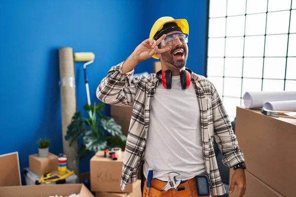 Young hispanic man with beard working at home renovation doing peace symbol with fingers over face, smiling cheerful showing victory