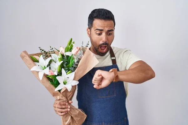 Hispanic man with beard working as florist looking at the watch time worried, afraid of getting late