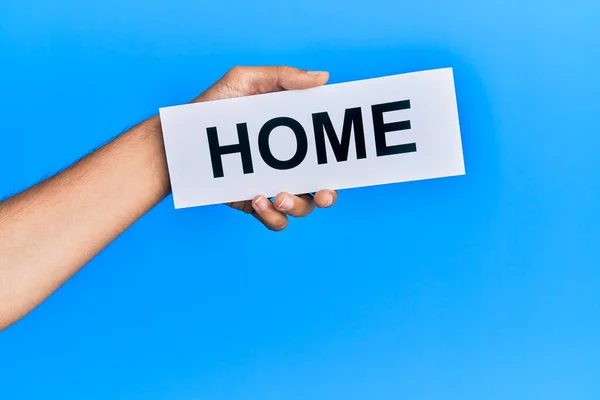 stock image Hand of caucasian man holding paper with home word over isolated blue background