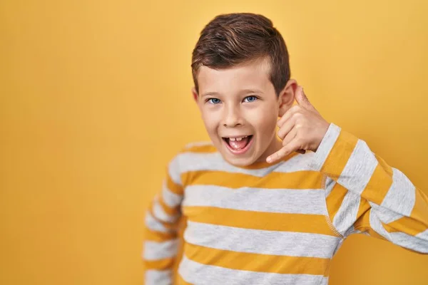 年轻的高加索小孩站在黄色的背景上微笑着 用手和手指做着电话手势 就像在电话里说话一样 交流概念 — 图库照片