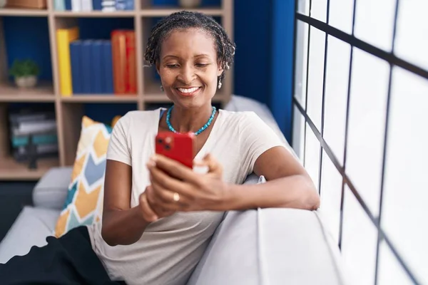Афроамериканська Жінка Середнього Віку Користуючись Смартфоном Сидить Дивані Вдома — стокове фото