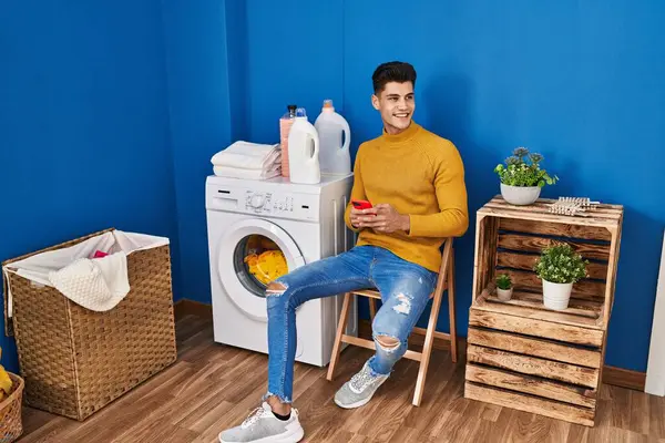 Young Hispanic Man Using Smartphone Waiting Washing Machine Laundry — Stockfoto
