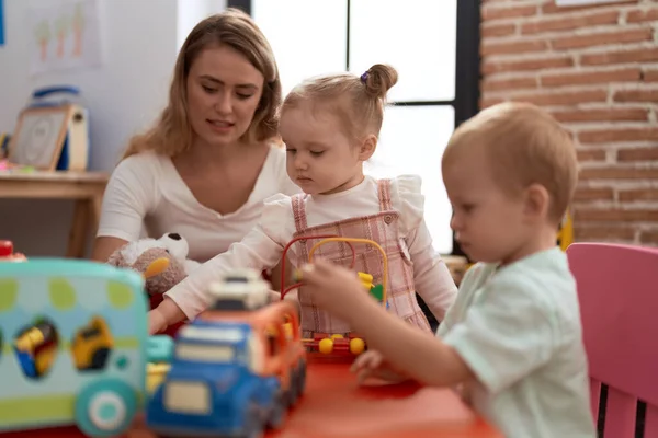 先生と男の子と女の子遊びおもちゃとテーブルの上に座って幼稚園 — ストック写真