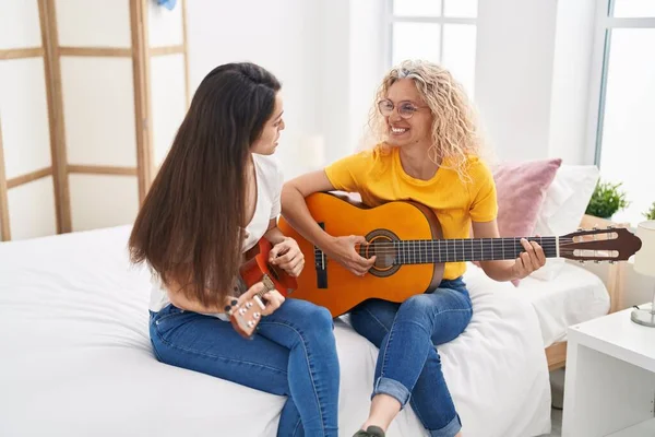 İki kadın anne ve kız yatak odasında klasik gitar ve ukulele çalıyorlar.