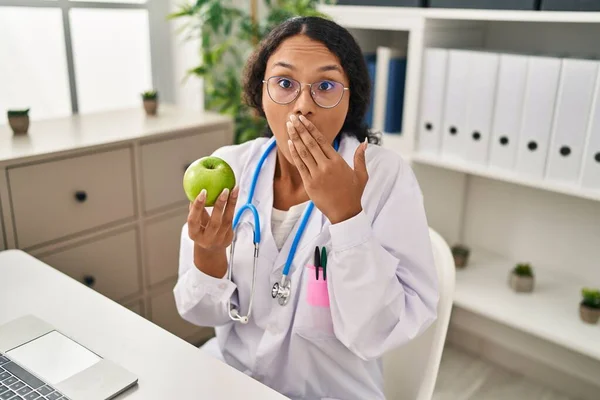 Young Hispanic Doctor Woman Holding Green Apple Covering Mouth Hand — Stock Photo, Image