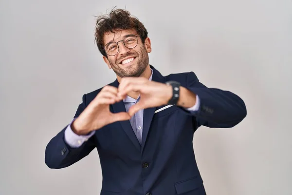 Hispanic business man wearing glasses smiling in love doing heart symbol shape with hands. romantic concept.
