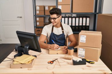 Latin kökenli genç bir iş adamı iş yerinde paket üzerine yazıyor.