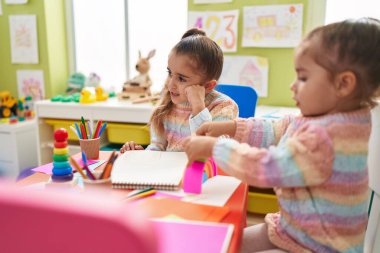 Two kids preschool students sitting on table drawing on paper at kindergarten
