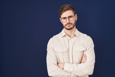 Hispanic man with beard standing over blue background skeptic and nervous, disapproving expression on face with crossed arms. negative person. 