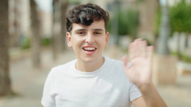 Non binary man smiling confident saying hello with hand at park