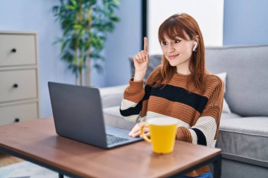 Young beautiful woman using computer laptop doing video call smiling with an idea or question pointing finger with happy face, number one 