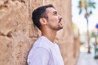 Young hispanic man looking to the sky with serious expression at street