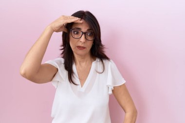 Middle age hispanic woman wearing casual white t shirt and glasses worried and stressed about a problem with hand on forehead, nervous and anxious for crisis 