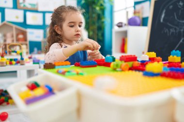 Adorable blonde girl playing with construction blocks sitting on table at kindergarten