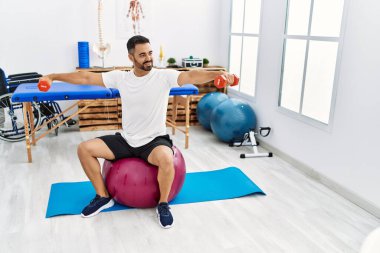 Genç İspanyol hasta, rehabilitasyon seansında sağlıklı top ve dambıllarla gülümsüyor.