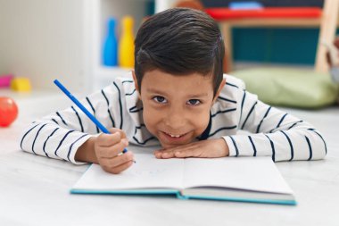 Anaokulunda defterine yazı yazan sevimli İspanyol çocuk.