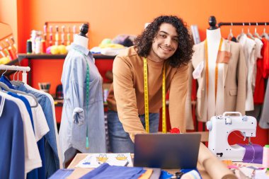 Genç Latin terzi atölyede dizüstü bilgisayar kullanarak gülümsüyor.