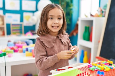 Anaokulundaki masada oturan, inşaat bloklarıyla oynayan sevimli İspanyol kız.