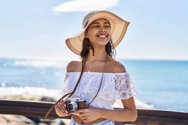 Genç Afro-Amerikan kadın turist deniz kenarında kamera kullanarak gülümsüyor.