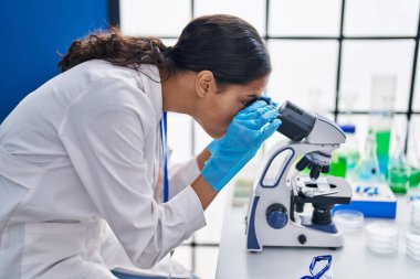 Genç Afrikalı Amerikalı kadın bilim adamı laboratuarda mikroskop kullanıyor.