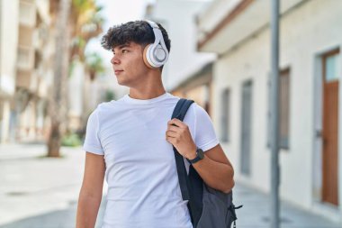 Young hispanic teenager student listening to music with relaxed expression at street