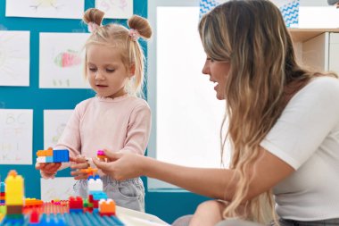 Teacher and toddler playing with construction blocks sitting on table at kindergarten