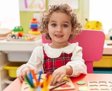 Adorable hispanic toddler playing with maths puzzle game sitting on table at kindergarten