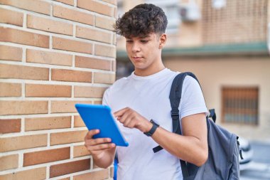 Young hispanic teenager student using touchpad with relaxed expression at street