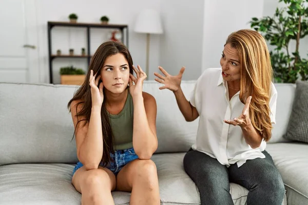 Mother and daughter unhappy arguing sitting on sofa at home
