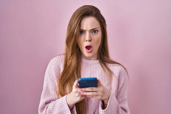 Young Caucasian Woman Using Smartphone Typing Message Shock Face Looking — Zdjęcie stockowe
