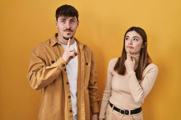 Young Hispanic Couple Standing Yellow Background Thinking Concentrated Doubt Finger — Stock Photo, Image