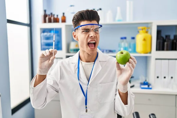 Young Hispanic Man Working Scientist Laboratory Holding Apple Angry Mad — ストック写真