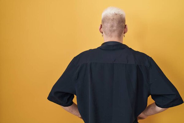 Молодой кавказский мужчина в солнечных очках, стоящий на желтом фоне, оглядываясь назад, с руками на теле. 