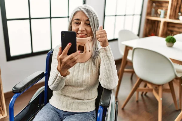 家で車椅子に座って電気通信をしている中年の白髪の女性 — ストック写真