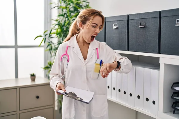 Hispanic doctor woman looking at the watch angry and mad screaming frustrated and furious, shouting with anger. rage and aggressive concept.